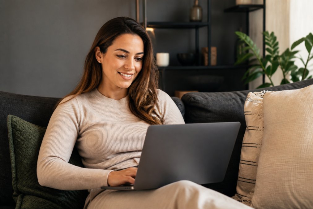 Persoon ontspannen thuis op een bank zittend met laptop, bladert door erotische webshop met gerichte interesse en een glimlach