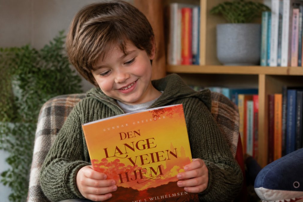 Et barn holder en vakker illustrert barneboka med hendene, smiler og ser ned på omslaget med interesse og nysgjerrighet