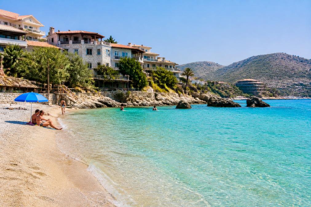 Een zonnig strand in Albanië met turquoise water en een paar vakantiegangers die ontspannen, met op de achtergrond authentieke mediterrane architectuur