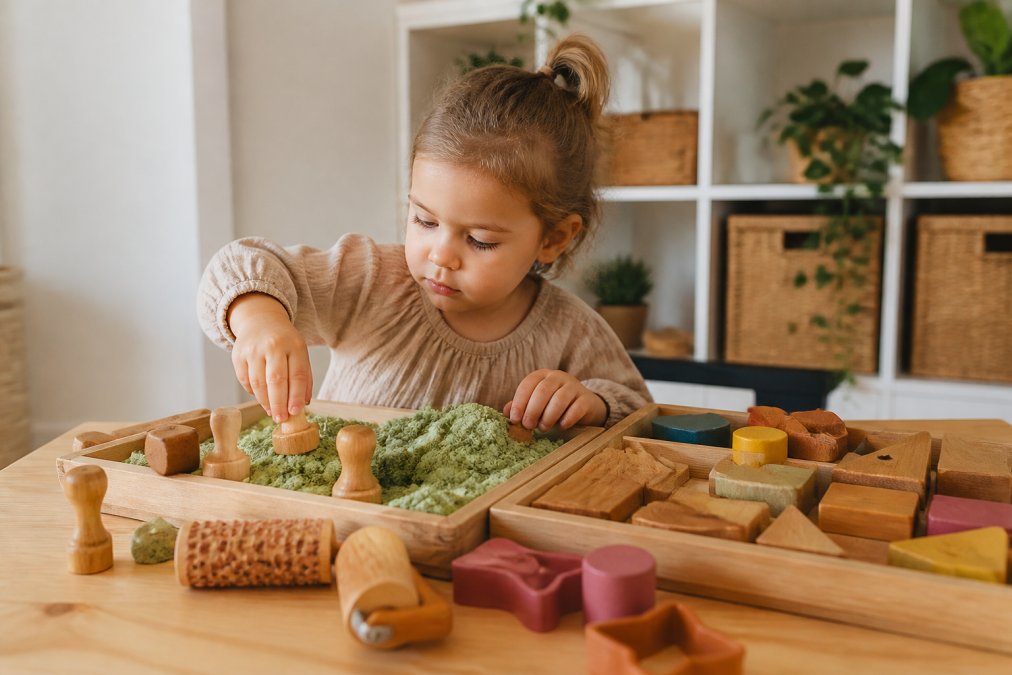 Peuter spelend met houten stempels en kinetisch zand, vormend en creatief werkend, met houten speelsets en rollers op tafel