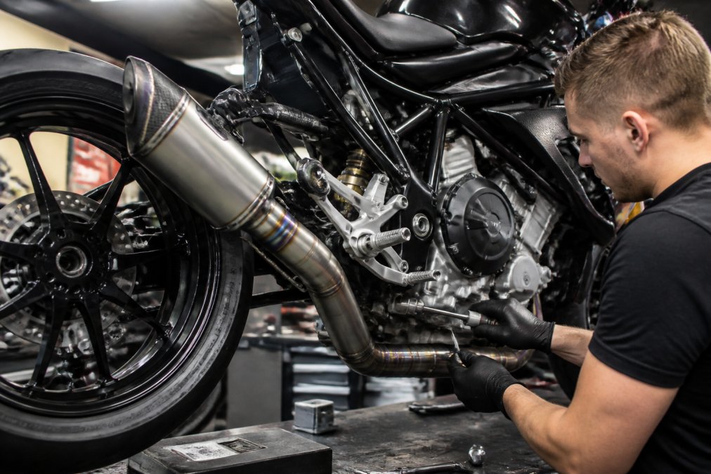 Professioneel gemonteerde titanium sportuitlaat op een high-end motorfiets in werkplaats, met zichtbare precisie-laswerk en karakteristieke glans van premium-materiaal onder werklampen
