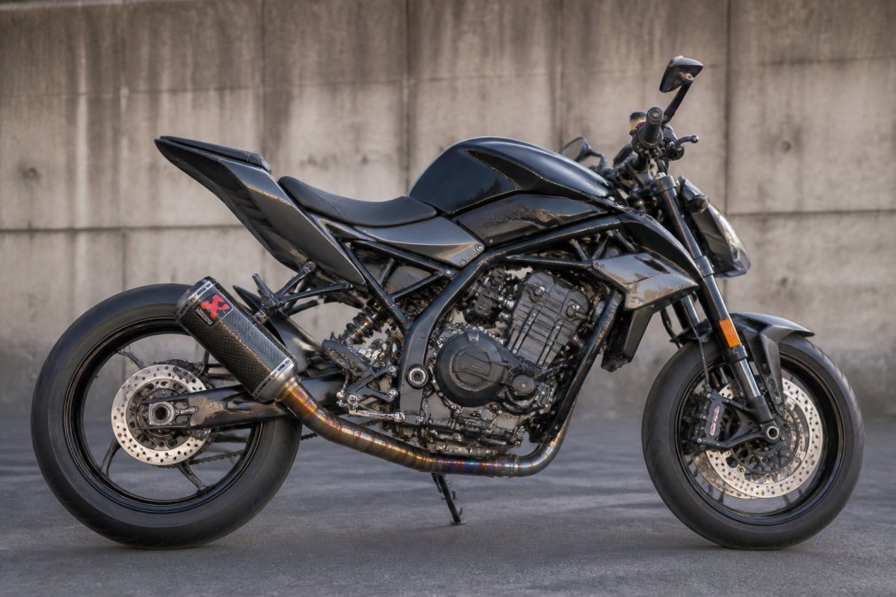 Yoshimura of Akrapovič carbon-uitlaatsysteem gemonteerd op een moderne sportmotor in zijkant weergave, met focus op de polished einddemper en manifolds
