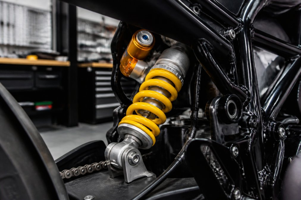 Close-up van een Ohlins-veersysteem op een sportmotor met focus op de schokdemper en ophanging in detail, met professionele werkplaatsverlichting