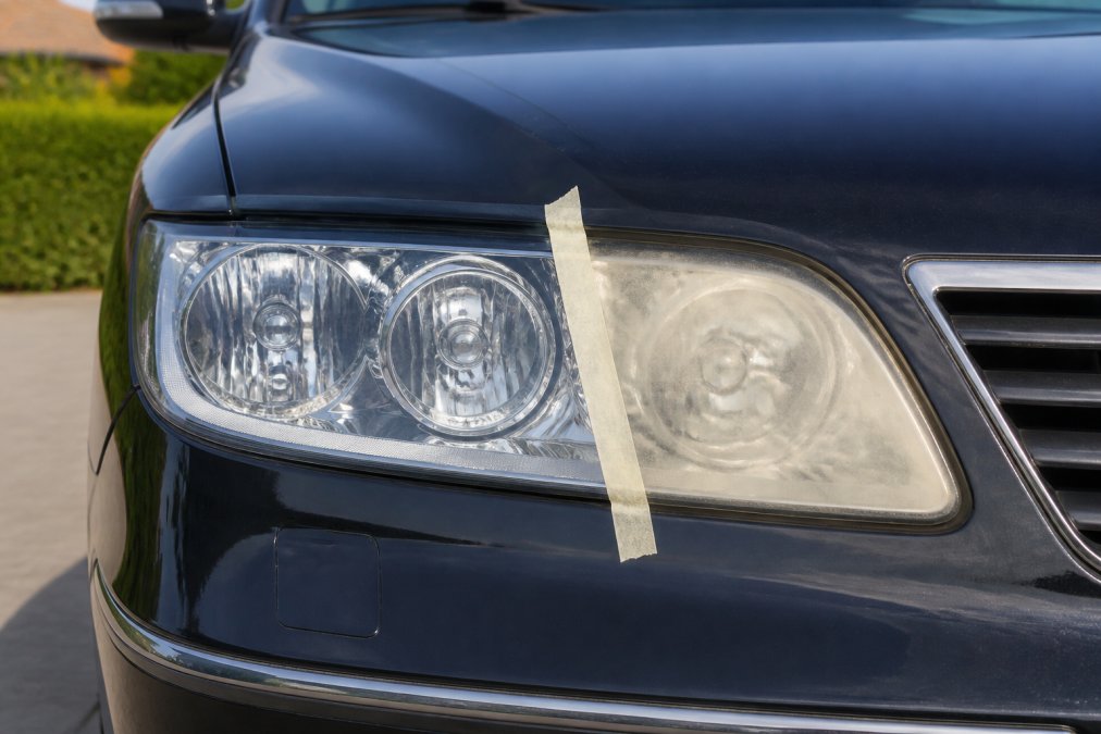 Twee koplampen naast elkaar in helder daglicht, de linker zijde glanzend en helder gepolijst met beschermlaag, de rechter zijde nog steeds dof en vergeeld zonder bescherming