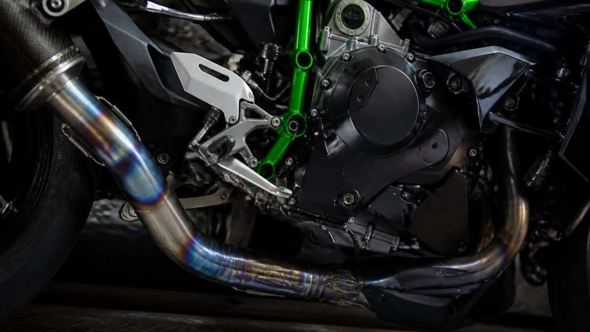 Close-up van een Kawasaki Ninja H2 supercharged motor met titanium uitlaatsysteem, zijkant in detail tegen donkere achtergrond