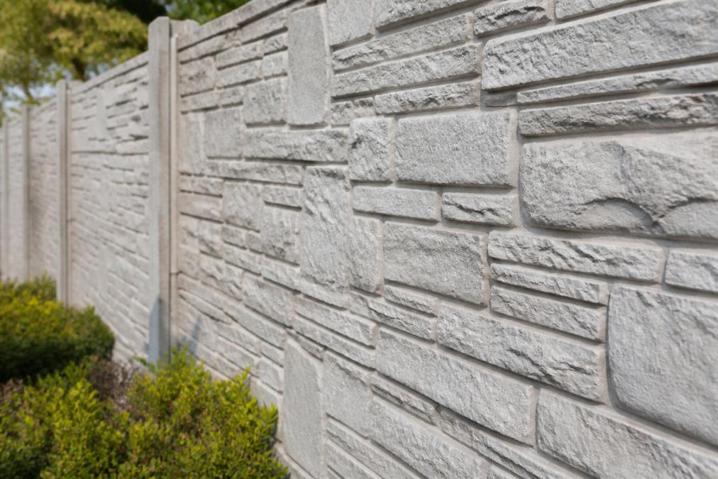 Close-up van een betonnen schutting met steenmotief textuur in zonlicht, waarbij de natuurlijke schaduwen en details van het patroon duidelijk zichtbaar zijn
