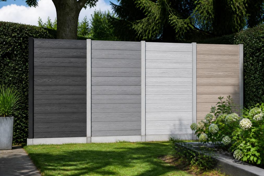 Vier betonnen schuttingpanelen in antraciet, grijs, wit en warmere tint naast elkaar in een groene tuinomgeving met daglicht, zodat kleurverschillen duidelijk zichtbaar zijn