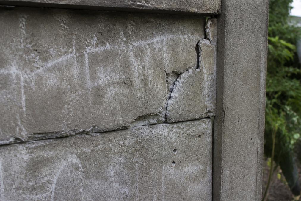 Close-up van beschadigde betonschutting met zichtbare scheuren, afbrokkeling en vorstschade in daglicht, oppervlakte toont wit efflorescentiepigment