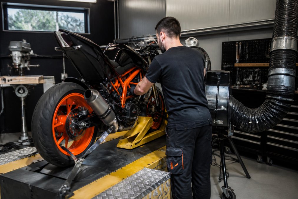 Gecertificeerde monteur in moderne werkplaats controleert motoronderdelen op professionele testbank met diagnostische apparatuur en computer-interface