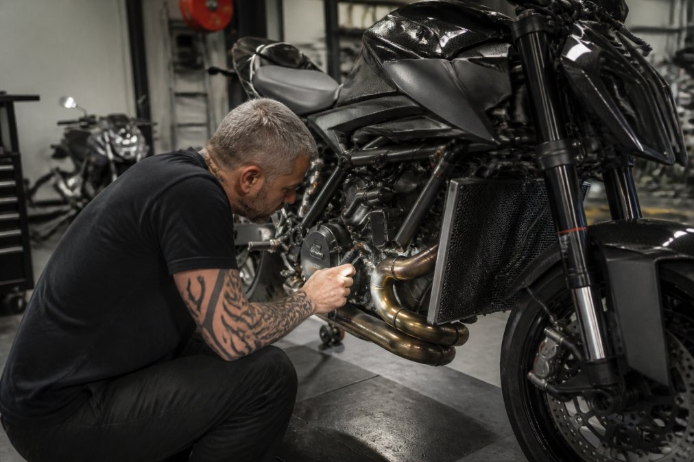 Ervaren motorrijder in werkplaats inspectert performance motorfiets met aandacht voor details, controleert chassis en motoronderdelen onder helder licht