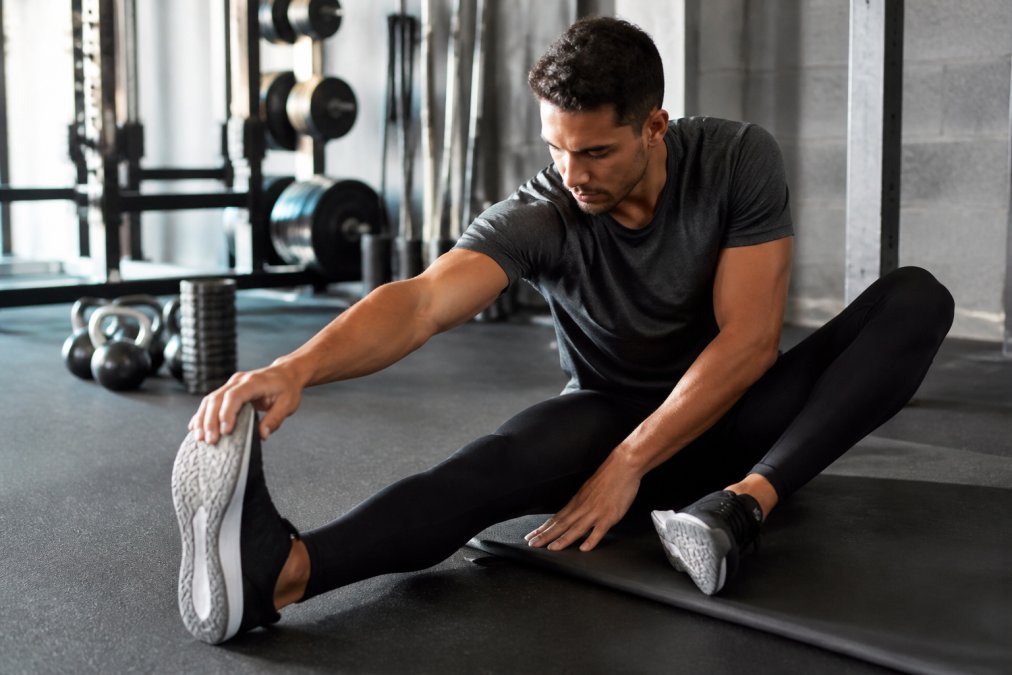 Athlete wearing compression leggings during post-workout stretching in a bright gym setting, demonstrating comfort and fit while recovering after intense training