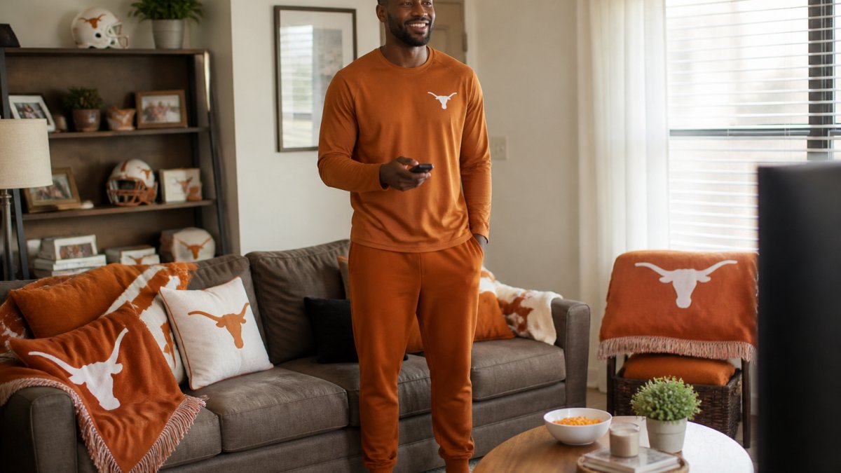 Tall man in a burnt orange long-sleeve shirt and joggers cheering for his team in a decorated living room