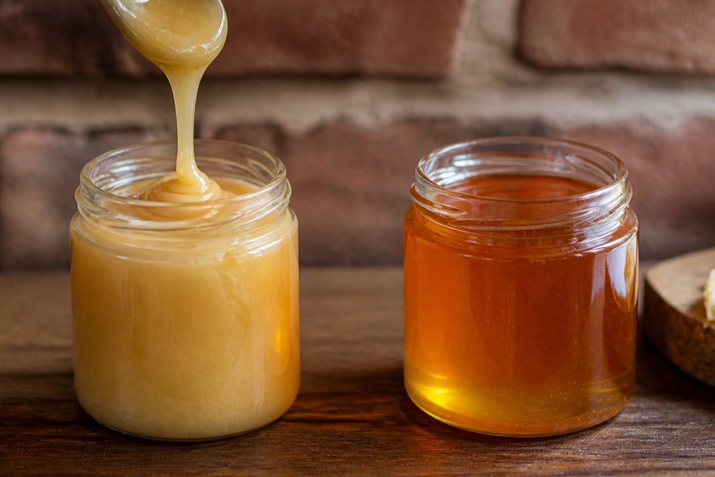 Nahaufnahme von frisch kaltgeschleudertem Honig, der golden in ein Glas fließt, sichtbare cremige Konsistenz, natürliche Farbe, Bienenwachspartikel