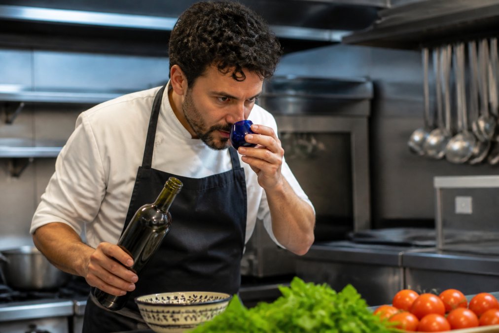 Professionele chef in restaurantkeuken die premium olijfolie proeft of giet, gericht en het product evaluerend