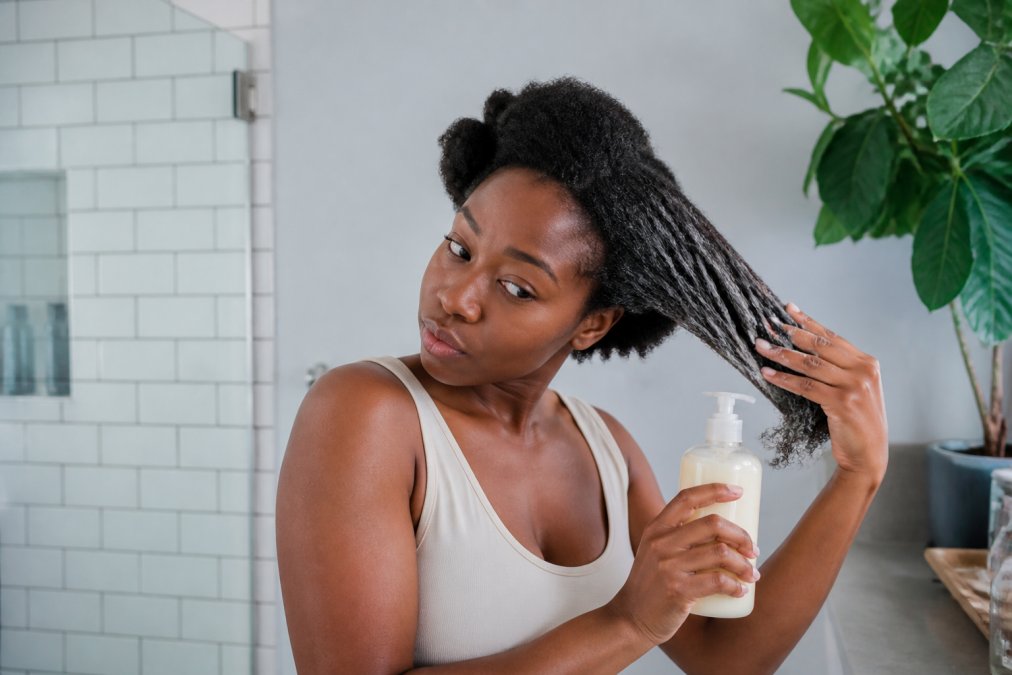 Black woman applying leave-in conditioner to 4C hair with products from a black owned beauty supply store.