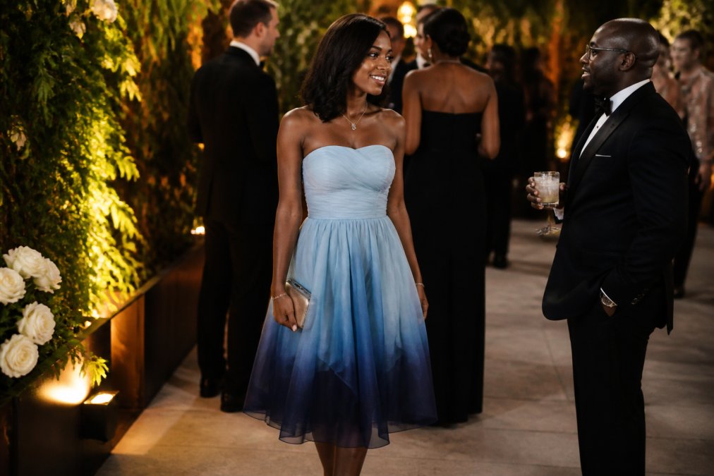 Woman wearing an elegant strapless ombré organza midi dress in soft-to-vibrant blue tones, standing with confident posture at an upscale evening wedding venue with warm ambient lighting