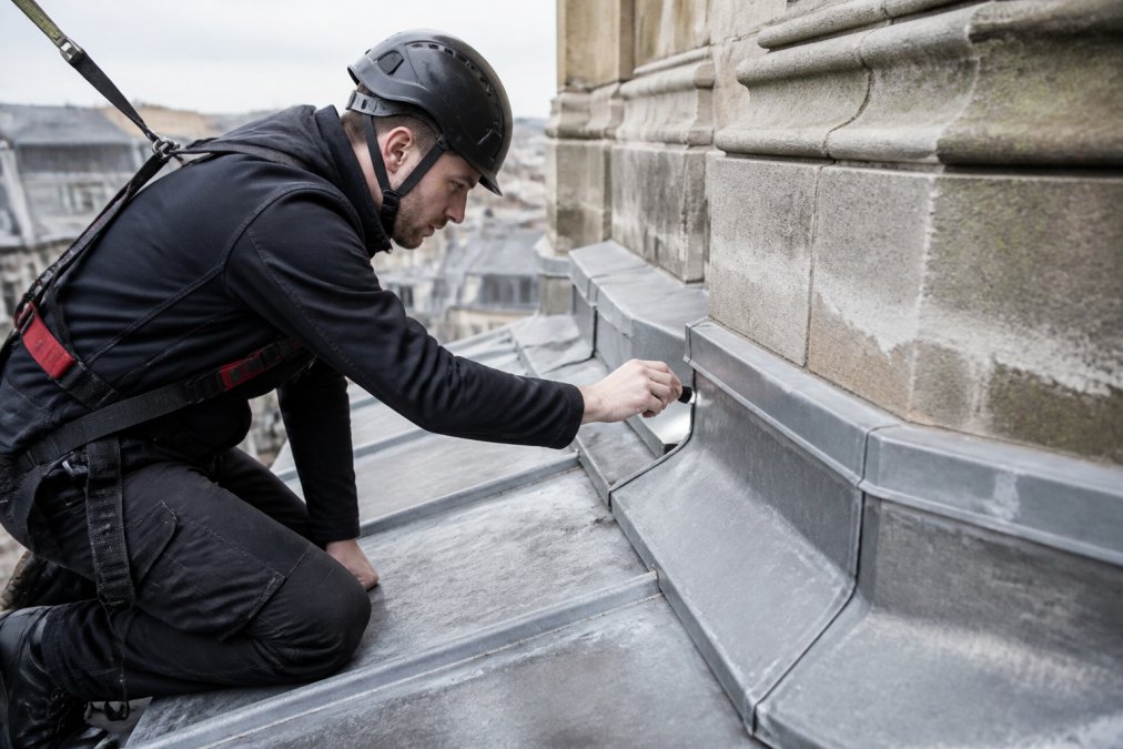 Dakdekker inspecteert historische loodwerk op monumentaal gebouw, onderhoudscontrole van oude loodbedekkingen met professionele inspectieapparatuur