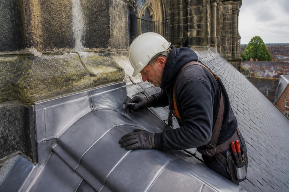 Dakdekker inspecteert historisch bladlood kwaliteit en duurzaamheid op een monumentaal gebouw met professionele apparatuur
