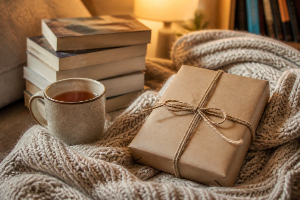 A hand-wrapped blind date book box resting on a cozy knit blanket beside a steaming mug of tea.