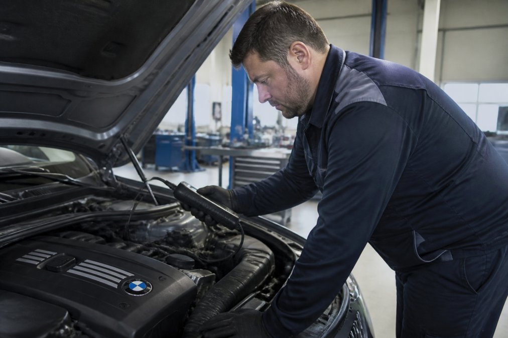 Master-certified technician connecting diagnostic scan equipment to a BMW engine, reviewing live sensor data on a computer screen in a modern repair facility