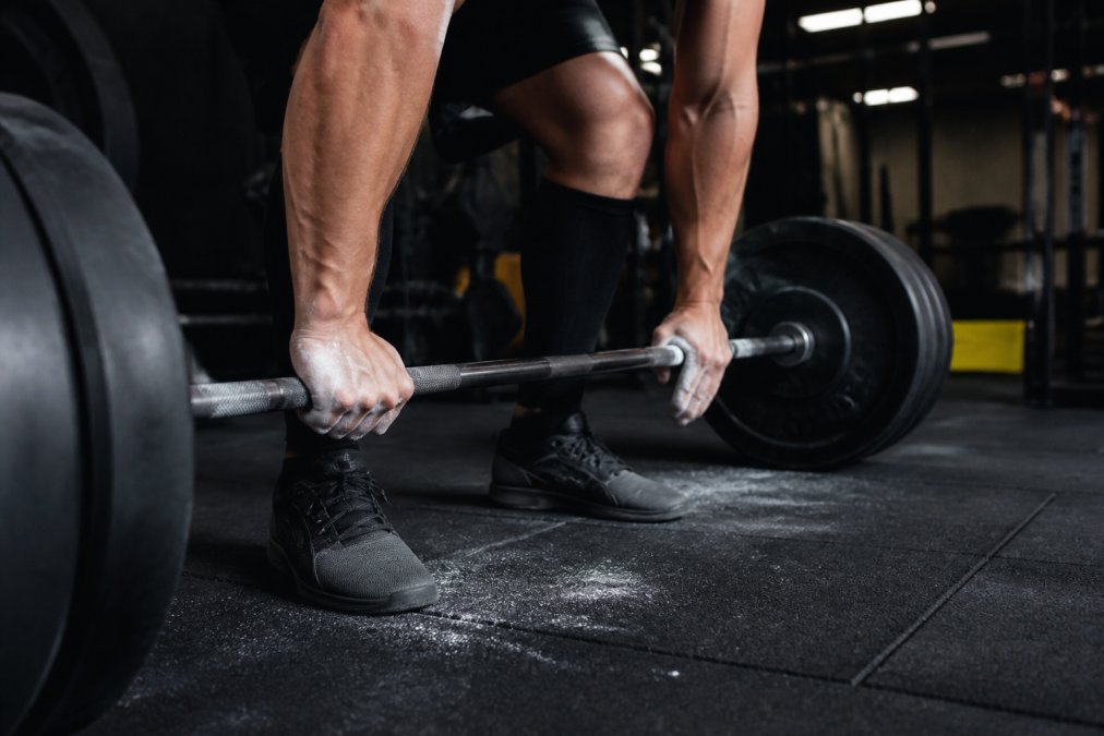 Lifter with chalked hands gripping a heavy barbell before taking bodybuilding supplements in the gym