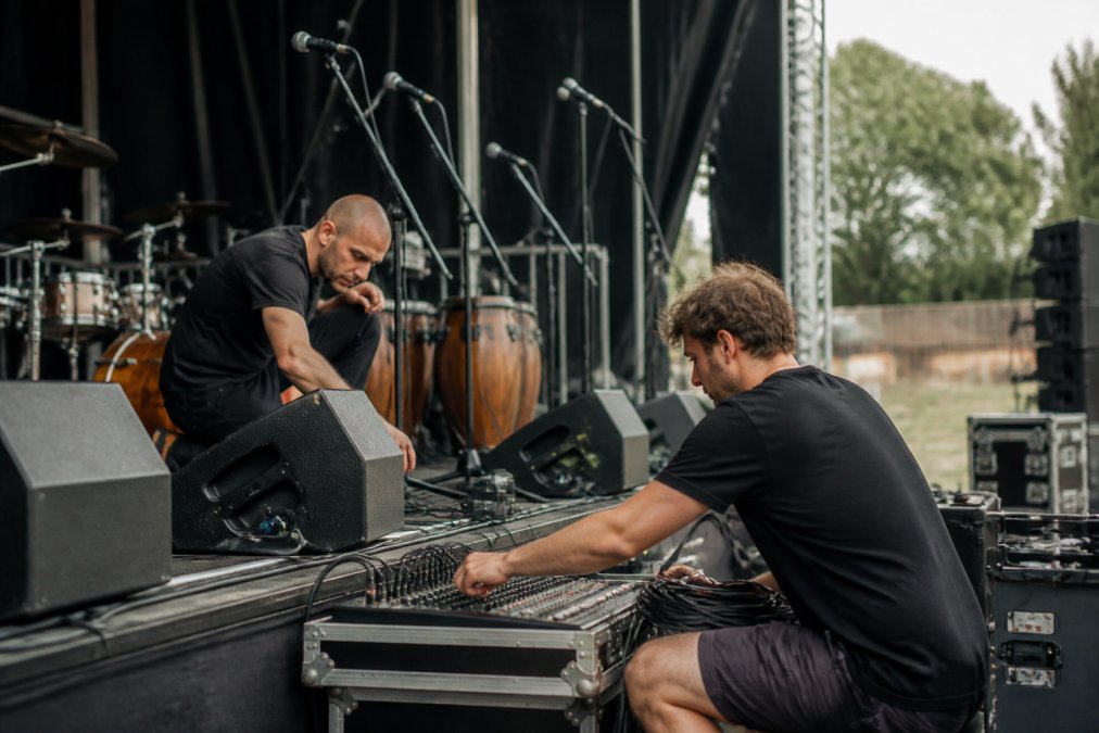 Muzikanten en geluidstechnicus die samen de geluidsinstallatie controleren op een podium voor een evenement, met microfoons en speakers zichtbaar
