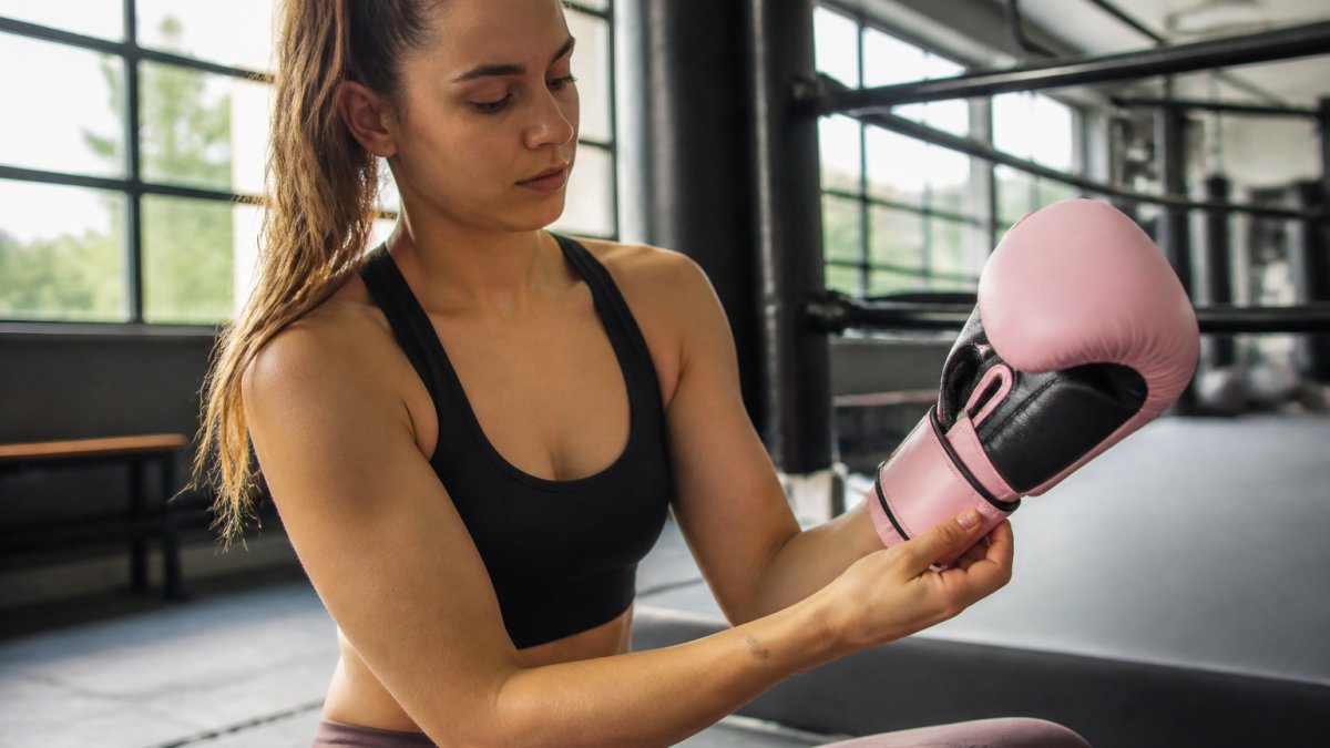 Vrouw die roze bokshandschoenen aantrekt en de pasvorm rond pols en hand controleert in een moderne trainingsruimte met natuurlijk licht
