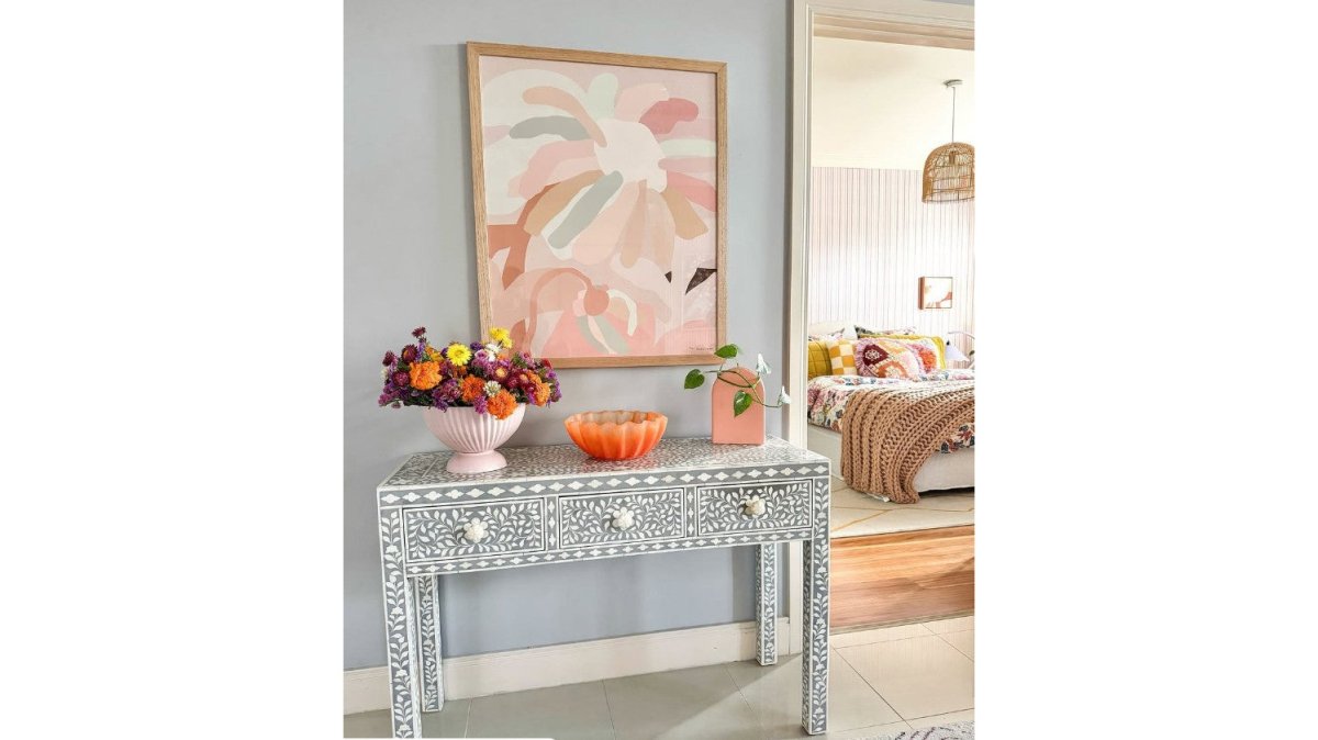 Close-up of a person using a soft microfiber cloth to gently dust the intricate floral bone inlay pattern on a grey console table in a bright living room