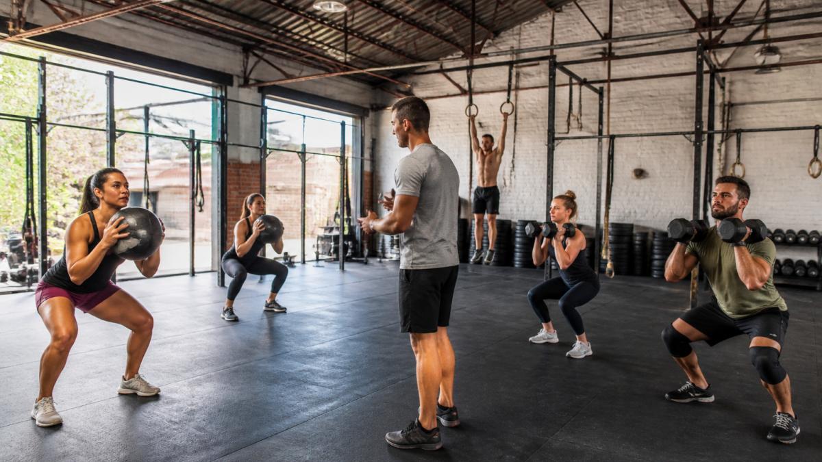Coach instructing a diverse group performing scaled movements during a book crossfit drop-in class.