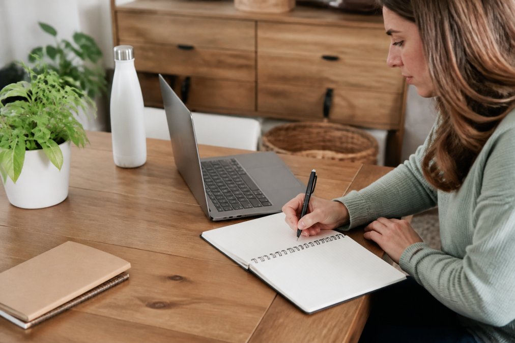 Person sitting at a desk with a health journal, pen, and water bottle, preparing notes for a virtual appointment on their laptop