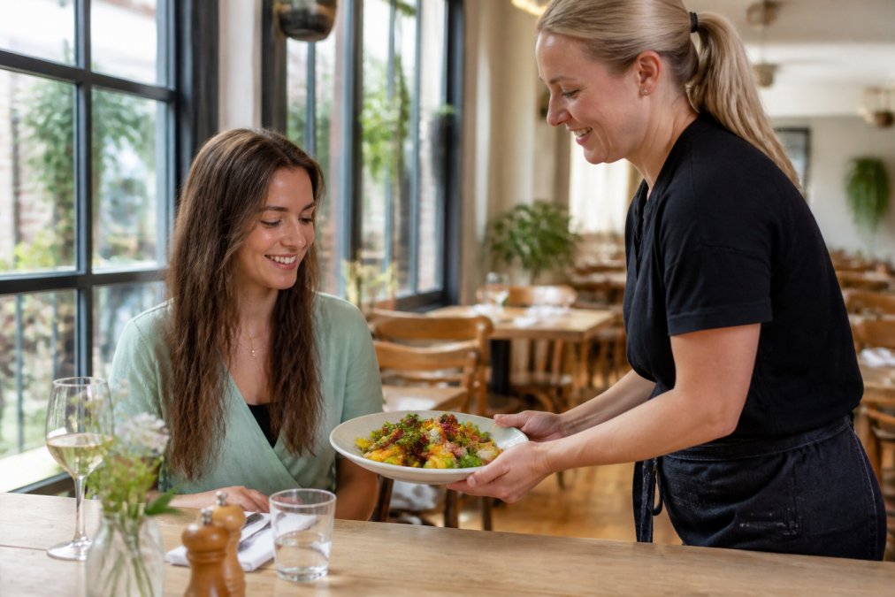 Restaurant staff presenting a beautifully plated vegan dish to a smiling diner, showcasing quality preparation and presentation, natural light highlighting the vibrant colours of the plate
