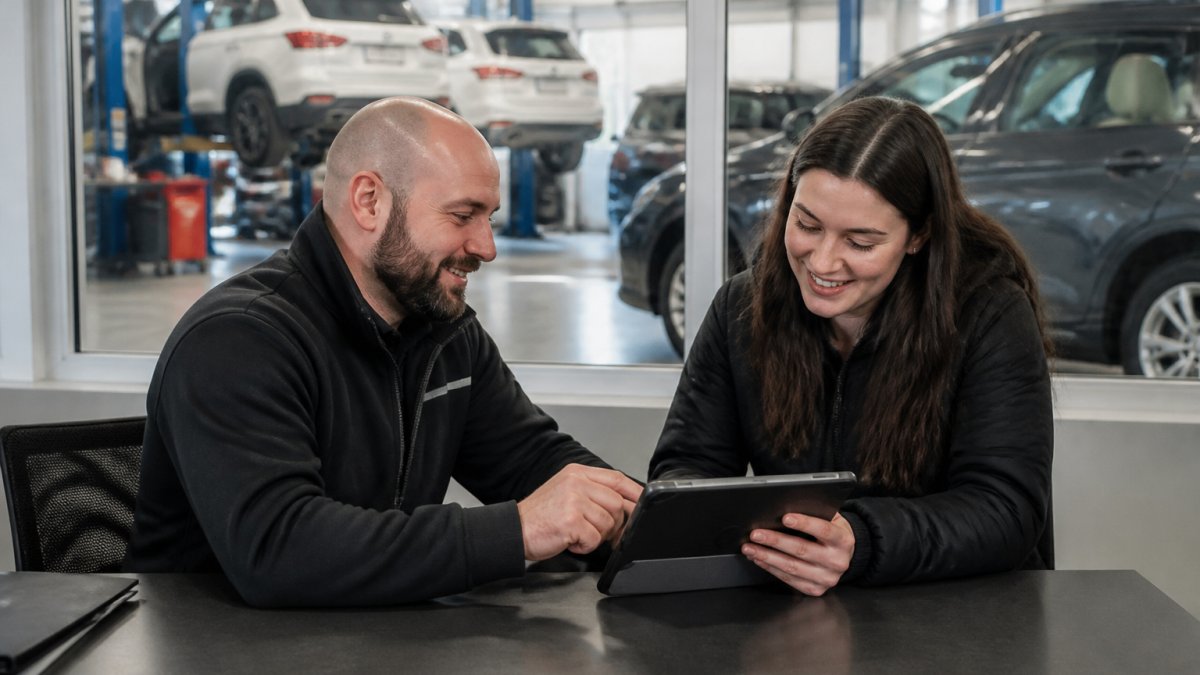 Service advisor assisting a customer with a vehicle service appointment on a tablet in a modern dealership office.
