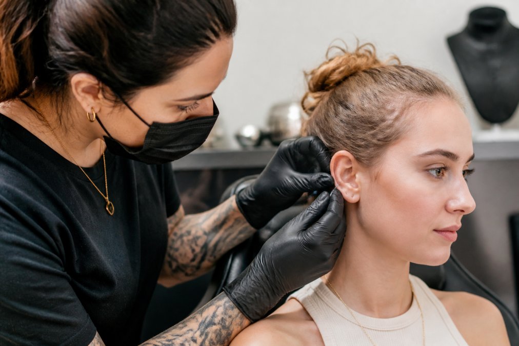 Professional piercer using a sterile needle during a calm ear piercing session in a clean studio.