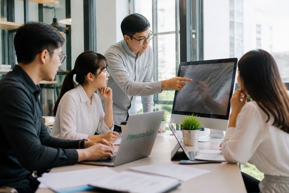 Team of e-commerce managers reviewing conversion metrics and workflow automation on a large monitor in modern office setting with natural lighting