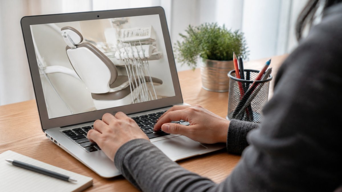 Close-up of hands typing on a laptop keyboard with a dental appointment booking form visible on screen, bright natural office lighting