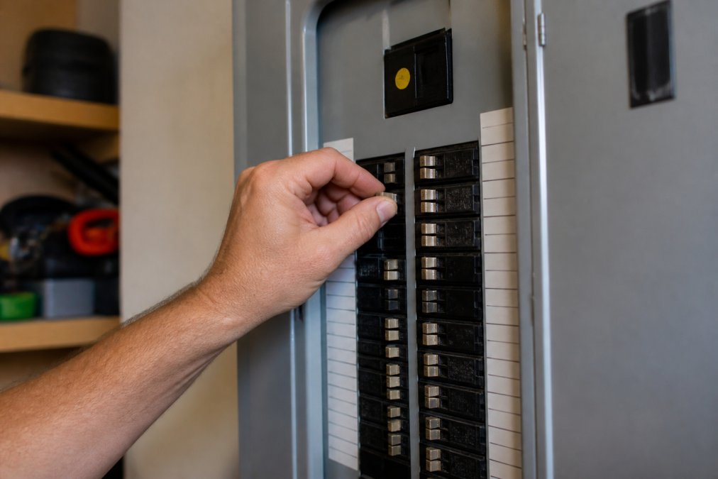 Professional electrician's hand safely turning off a circuit breaker in a residential electrical panel, showing clear labeling and proper technique with natural lighting