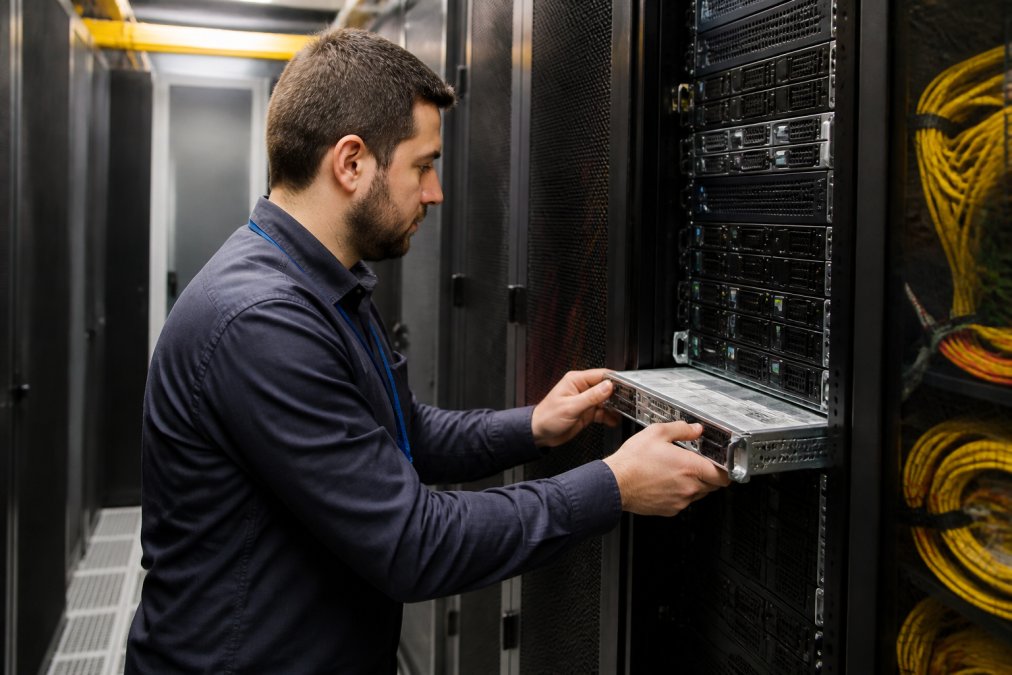 IT professional conducting a network assessment, examining server equipment and monitoring systems in a data center with multiple screens displaying network diagnostics
