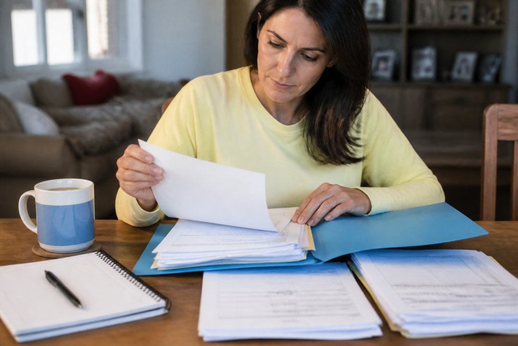 Patient sitting at a desk organizing medical documents and health records in a folder, with a cup of tea and notepad nearby