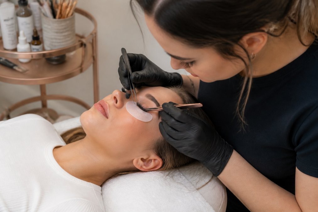 Lash artist applying lash extensions in Mystic to a client relaxing in a bright, professional studio.