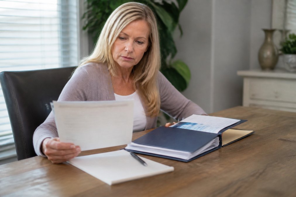 Patient sitting at a desk reviewing medical documents and preparing a folder with health records, with a notepad and pen nearby