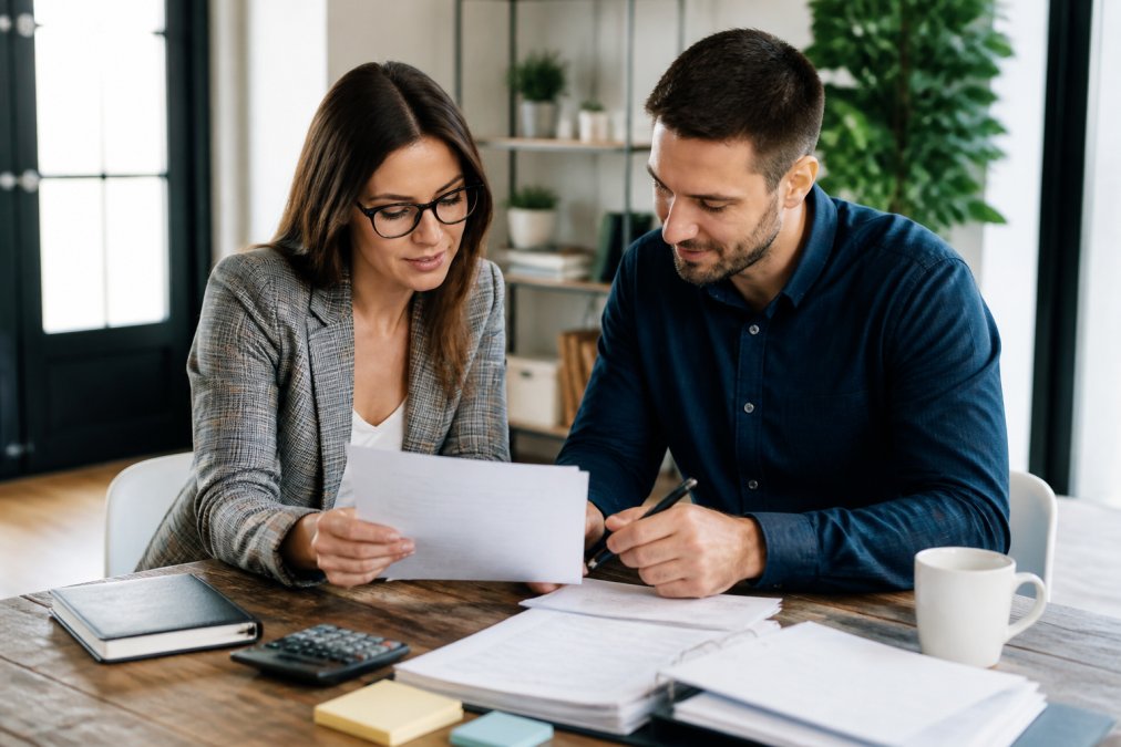 A professional bookkeeper and a small business owner sitting across from each other at a table, reviewing printed financial statements together in a friendly meeting