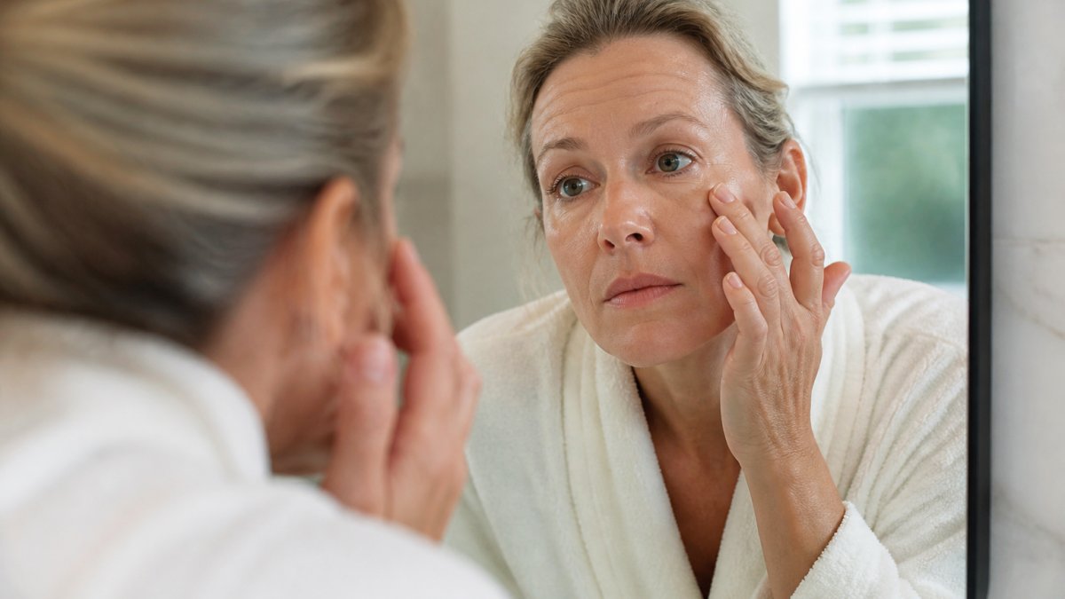 A woman in her forties examining the fine lines under her eyes in a well-lit bathroom mirror, soft natural light, calm and reflective mood
