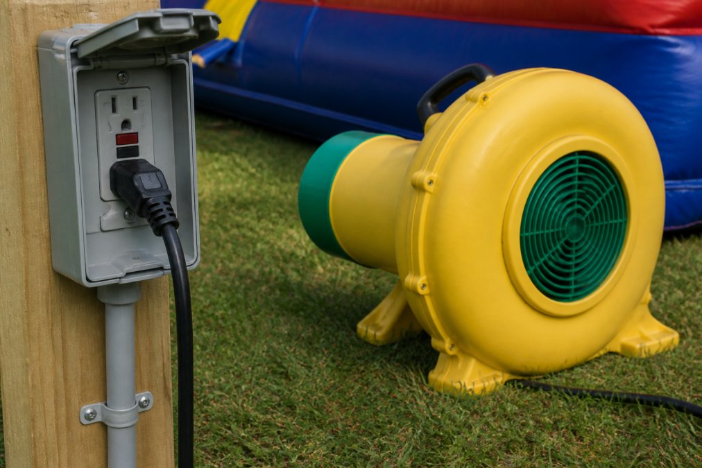 Close-up of electrical outlet with GFCI protection switch and properly grounded power cord connected to bounce house blower unit outdoors