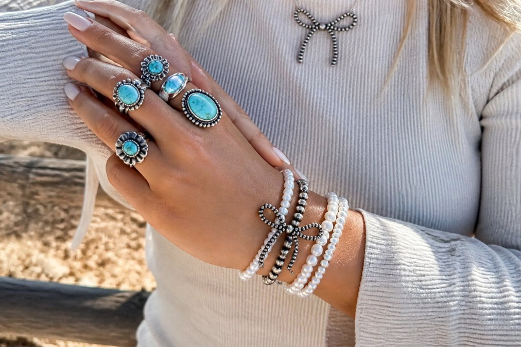 Close-up of stacked turquoise rings and pearl bracelets on a woman's hands, showcasing multiple jewelry pieces layered together with natural sunlight highlighting the silver and turquoise tones
