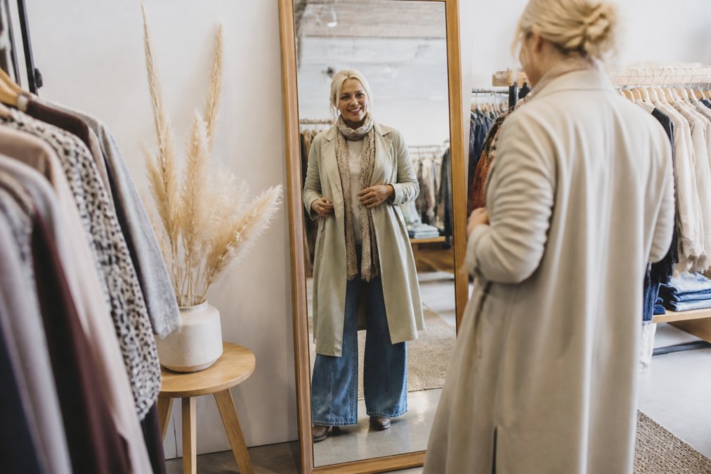 Woman examining layered outfits in a mirror during a boutique fashion styling session