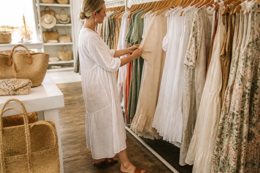 Woman browsing linen dresses and woven accessories during a boutique shopping trip in a bright, airy store.