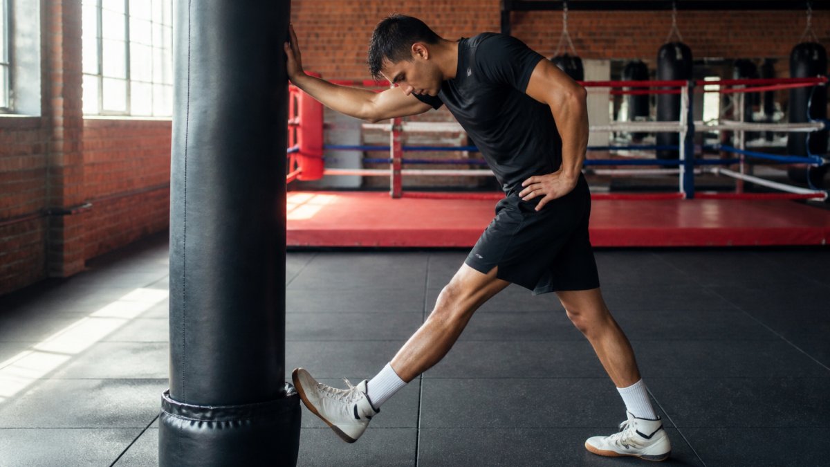 Boxer performing a hamstring stretch against a heavy bag for boxing recovery tips