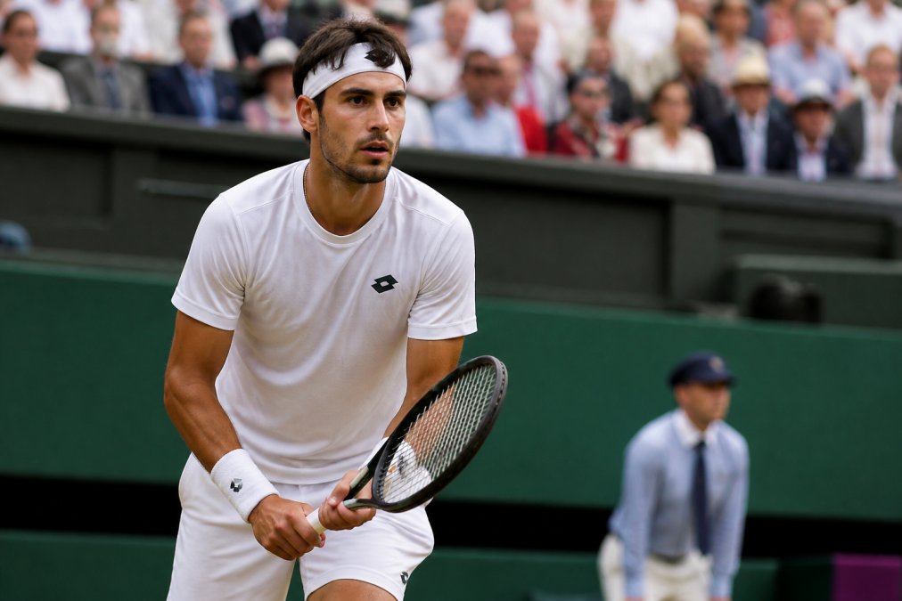 Tennis player at the baseline during a competitive match with focused expression and composed body language, showing mental concentration during a high-pressure moment in bright stadium lighting