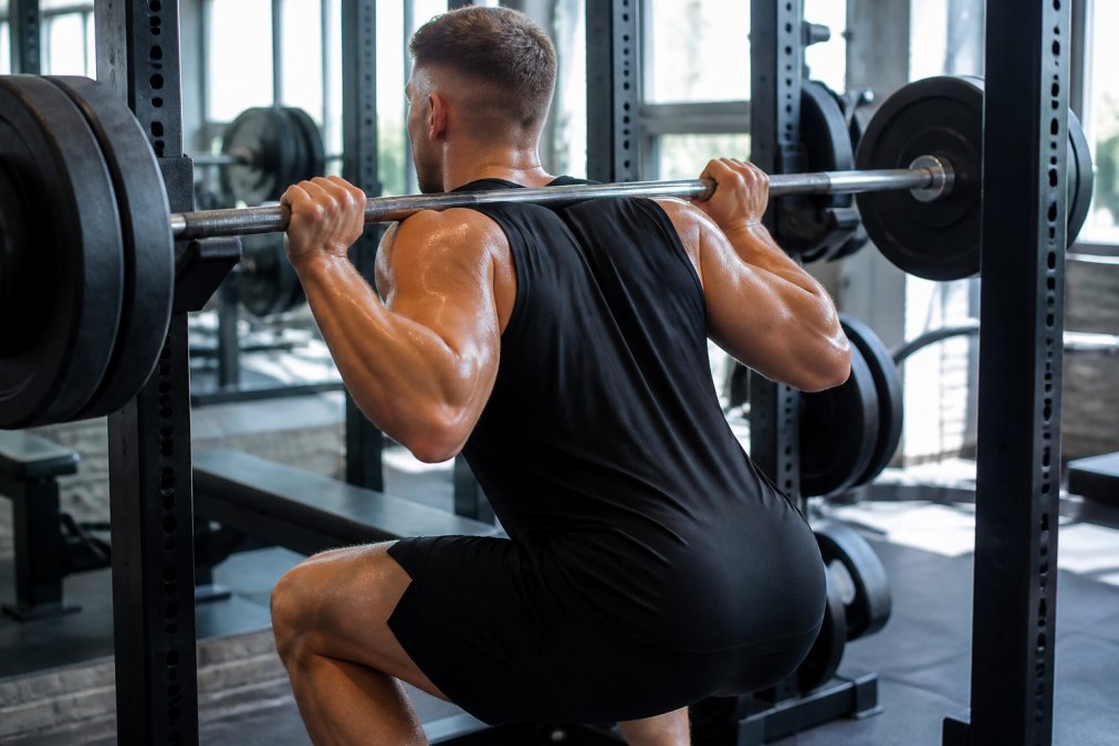Muscular man performing squats in breathable gym wear that stays dry during an intense workout session.