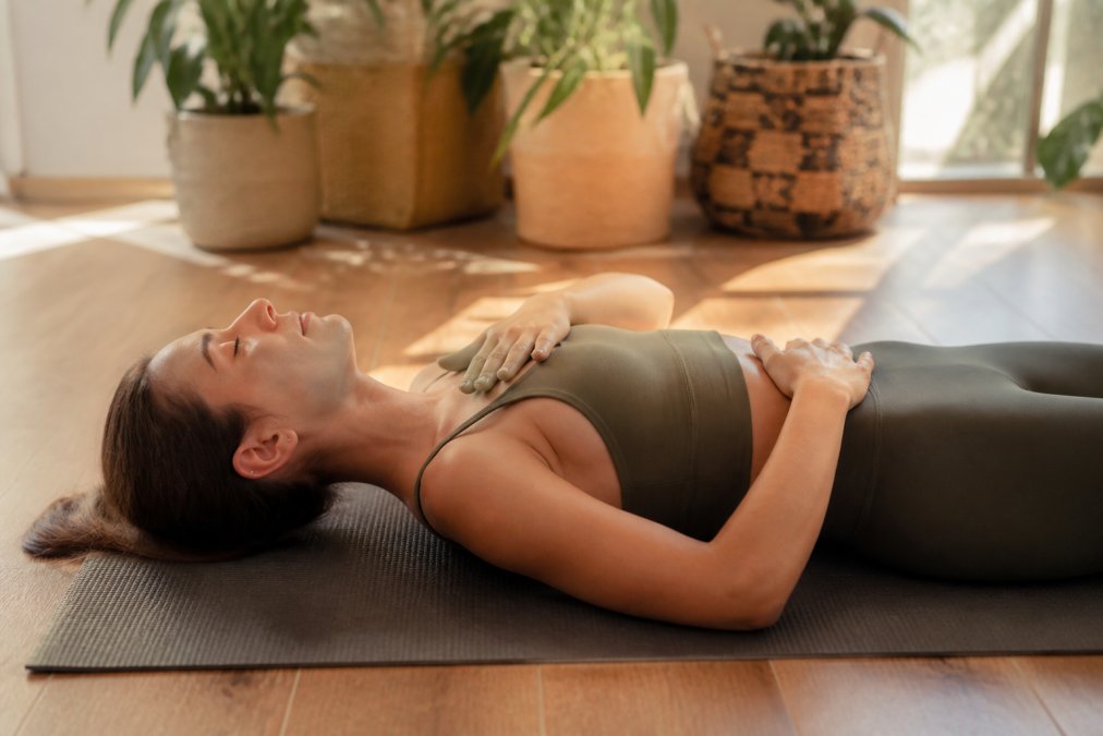 Woman practicing diaphragmatic breathing as part of her breathwork techniques while lying on a yoga mat.